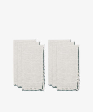 Six folded beige Nico Napkins with dark green stitched edges, arranged in two stacks against a white backgroundâ€”modern, elegant table linens ideal for dining.