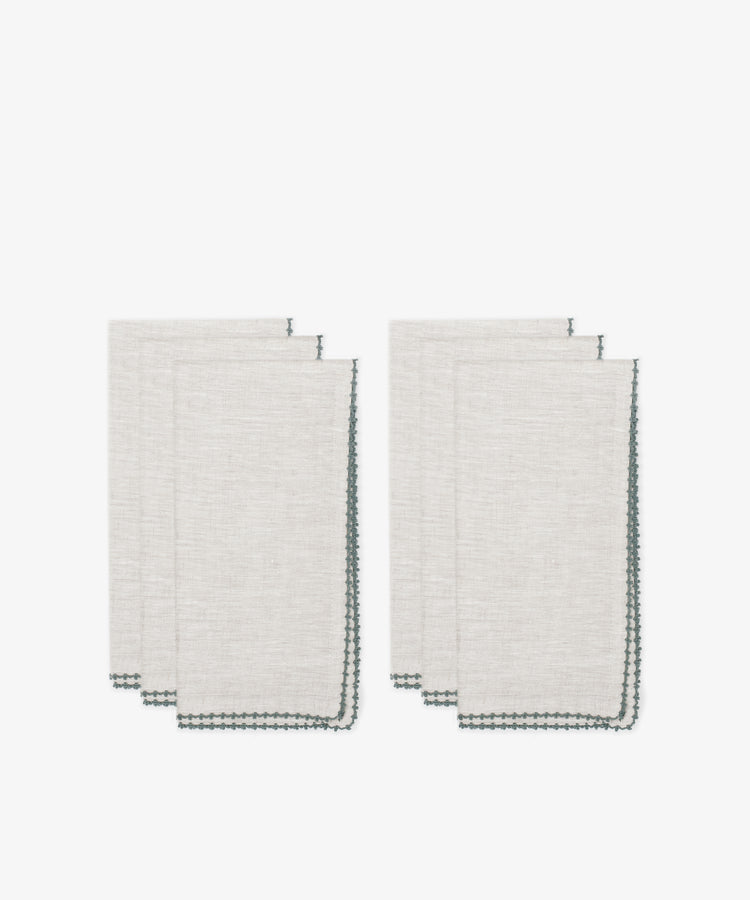 Six folded beige Nico Napkins with dark green stitched edges, arranged in two stacks against a white background—modern, elegant table linens ideal for dining.