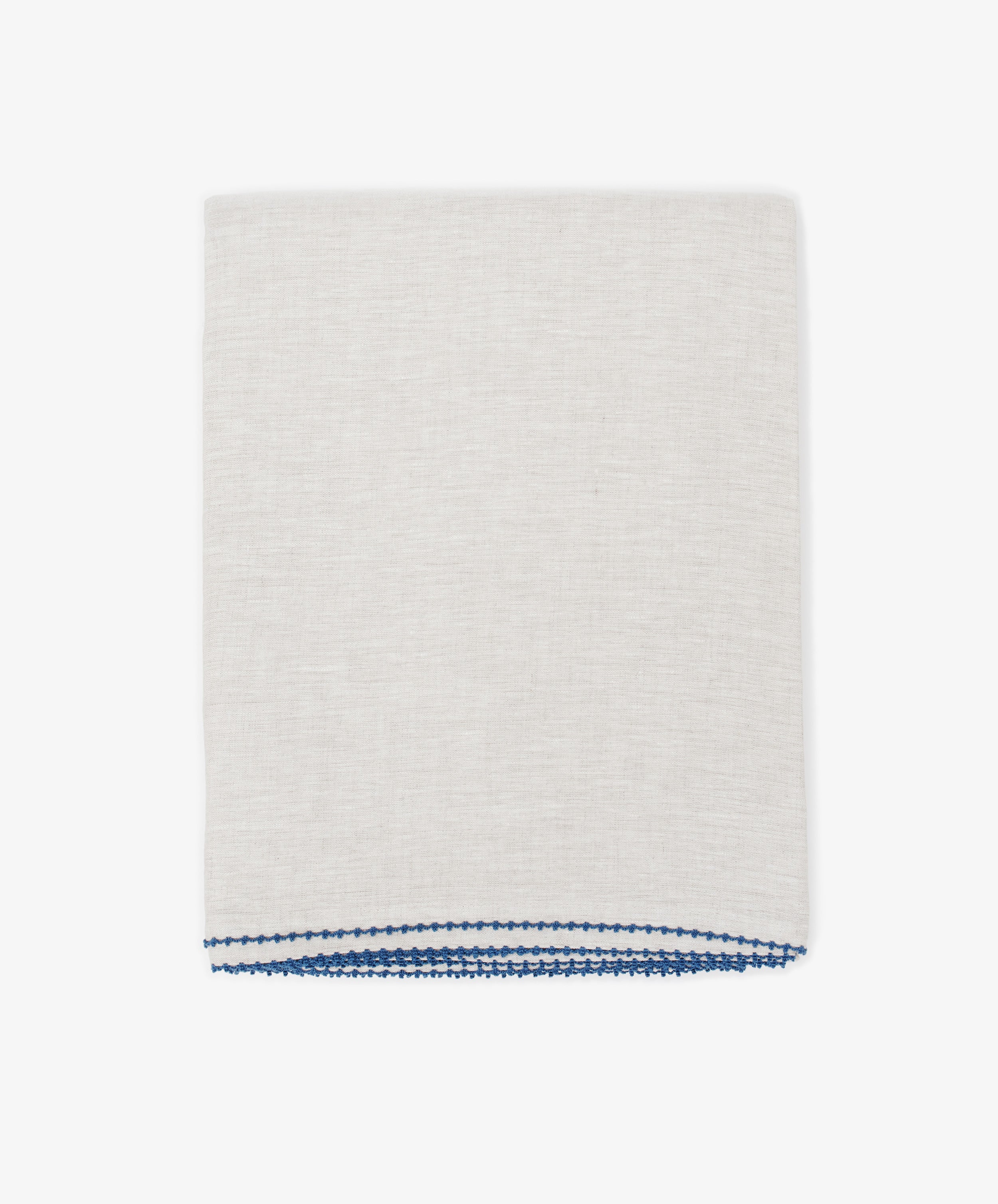 The Nico Tablecloth, in light beige linen with blue stitching along one edge, is neatly folded and hand-stitched, shown against a plain white background.