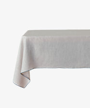 The Nico Tablecloth, a plain light-colored linen, is draped over a rectangular table set against a white background.
