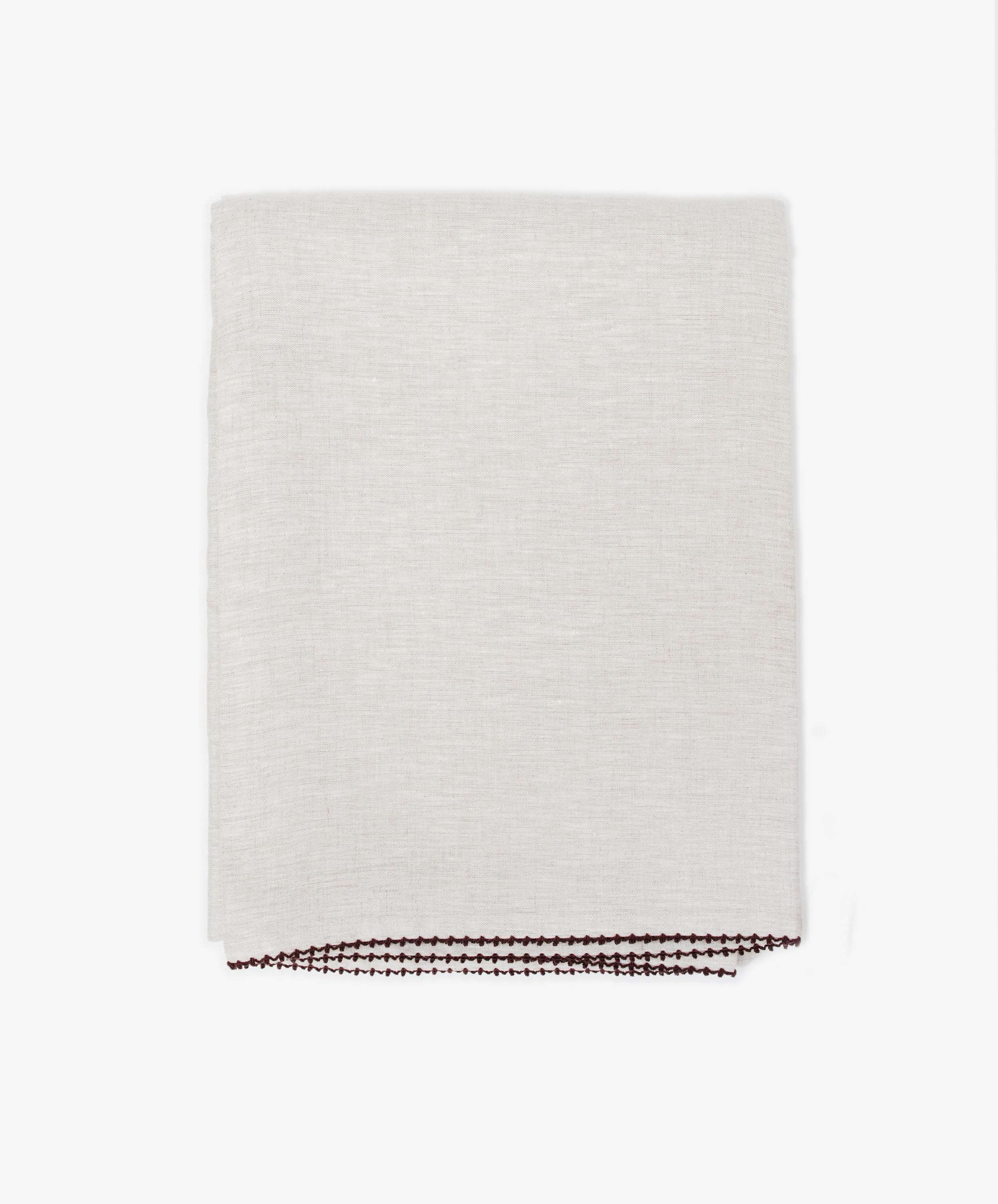 The Nico Tablecloth features light-colored, subtly textured fabric with dark hand-stitched detailing along the edge—perfect for elegant table linens.