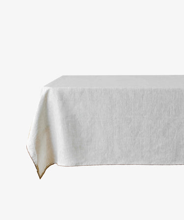 A rectangular table with the Nico Tablecloth, a plain white linen cover, draped so that one corner hangs lower than the others.