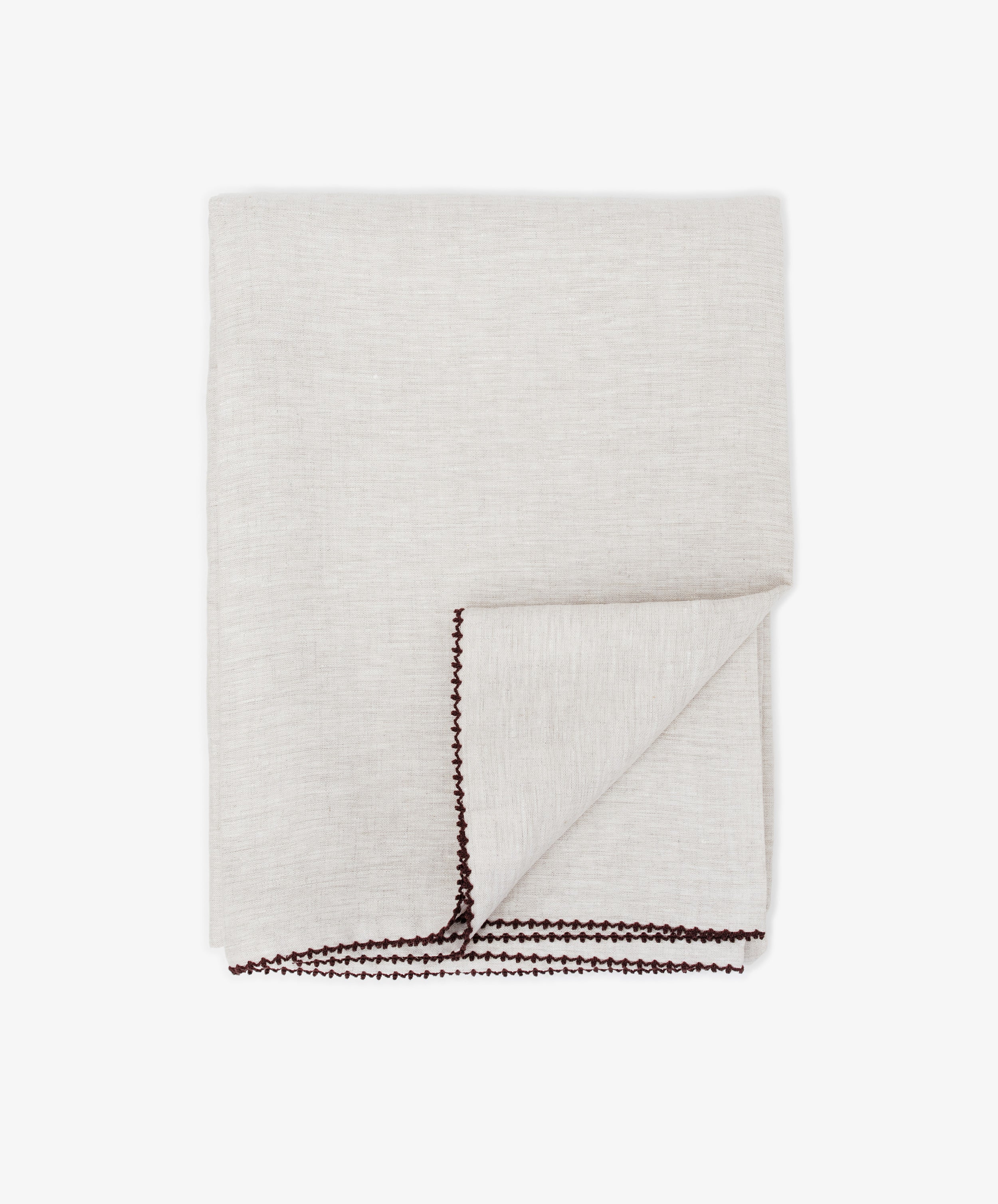 The Nico Tablecloth is a neatly folded light beige linen tablecloth with dark brown hand-stitched edges, displayed on a white background.