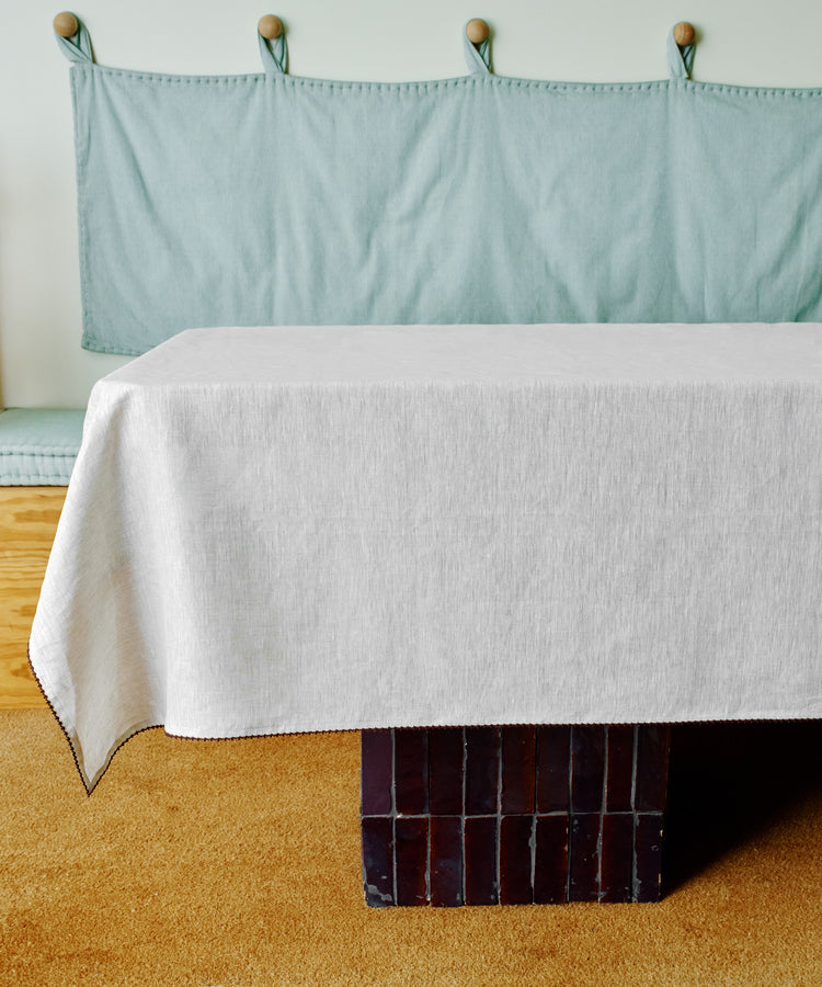 A rectangular table draped with the Nico Tablecloth stands before a cushioned bench with a light blue fabric backrest, offering an inviting setting for creative table decor.