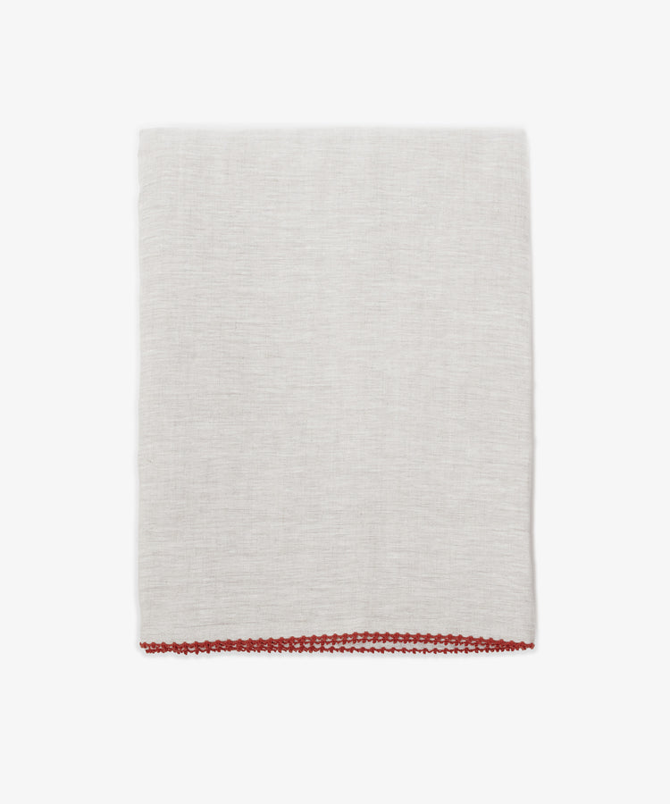 The Nico Tablecloth, in light gray linen with hand stitching and a red border along the bottom edge, is shown folded on a plain white background.
