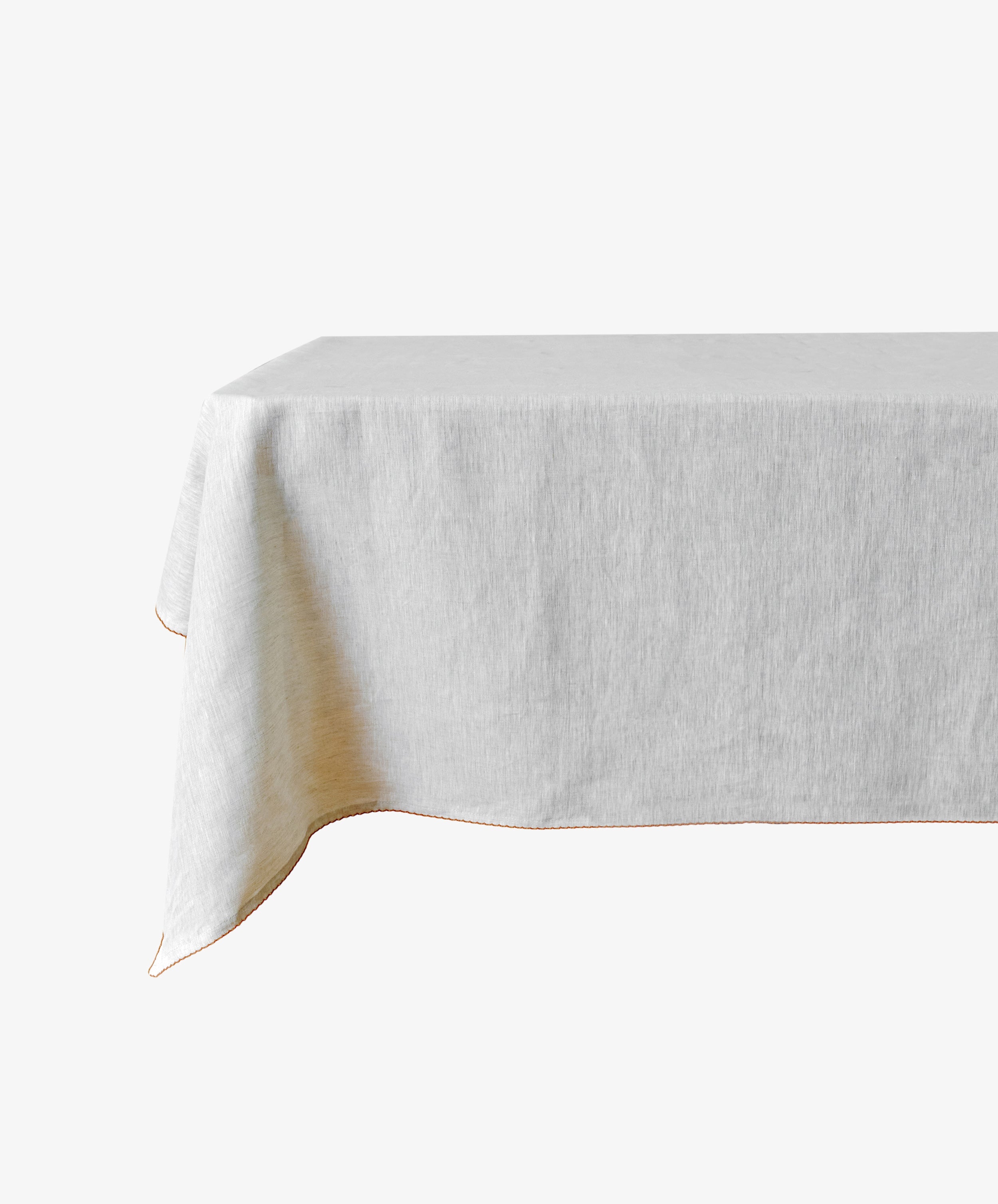 A rectangular table covered with the Nico Tablecloth—a plain, light-colored linen—set against a white background.