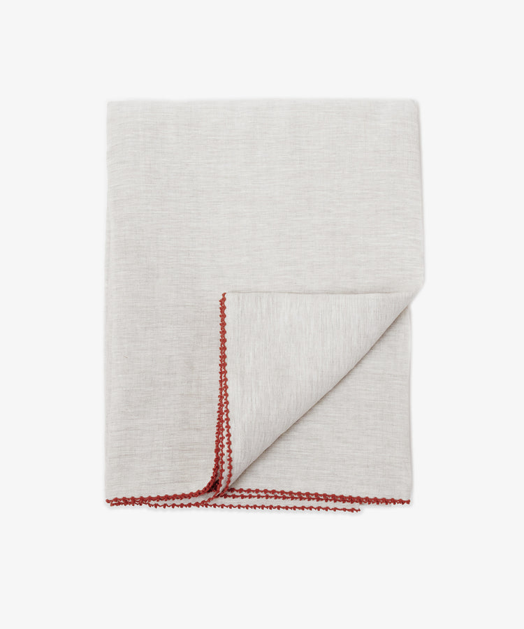 The Nico Tablecloth in light gray features a red hand-stitched border along the edges—an elegant detail that adds sophistication to your table setting.