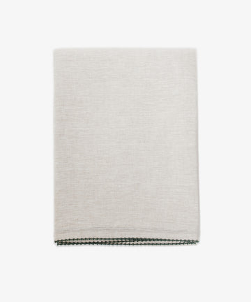 The Nico Tablecloth is a light beige linen with subtle texture and thin dark hand-stitched edging, neatly folded and perfect for elegant tables, set against a white background.