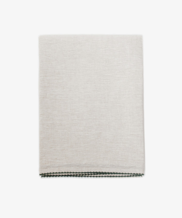 The Nico Tablecloth is a light beige linen with subtle texture and thin dark hand-stitched edging, neatly folded and perfect for elegant tables, set against a white background.