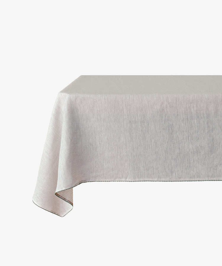 A rectangular table draped with the Nico Tablecloth, a light gray linen featuring subtle hand-stitched detail, set against a white background.