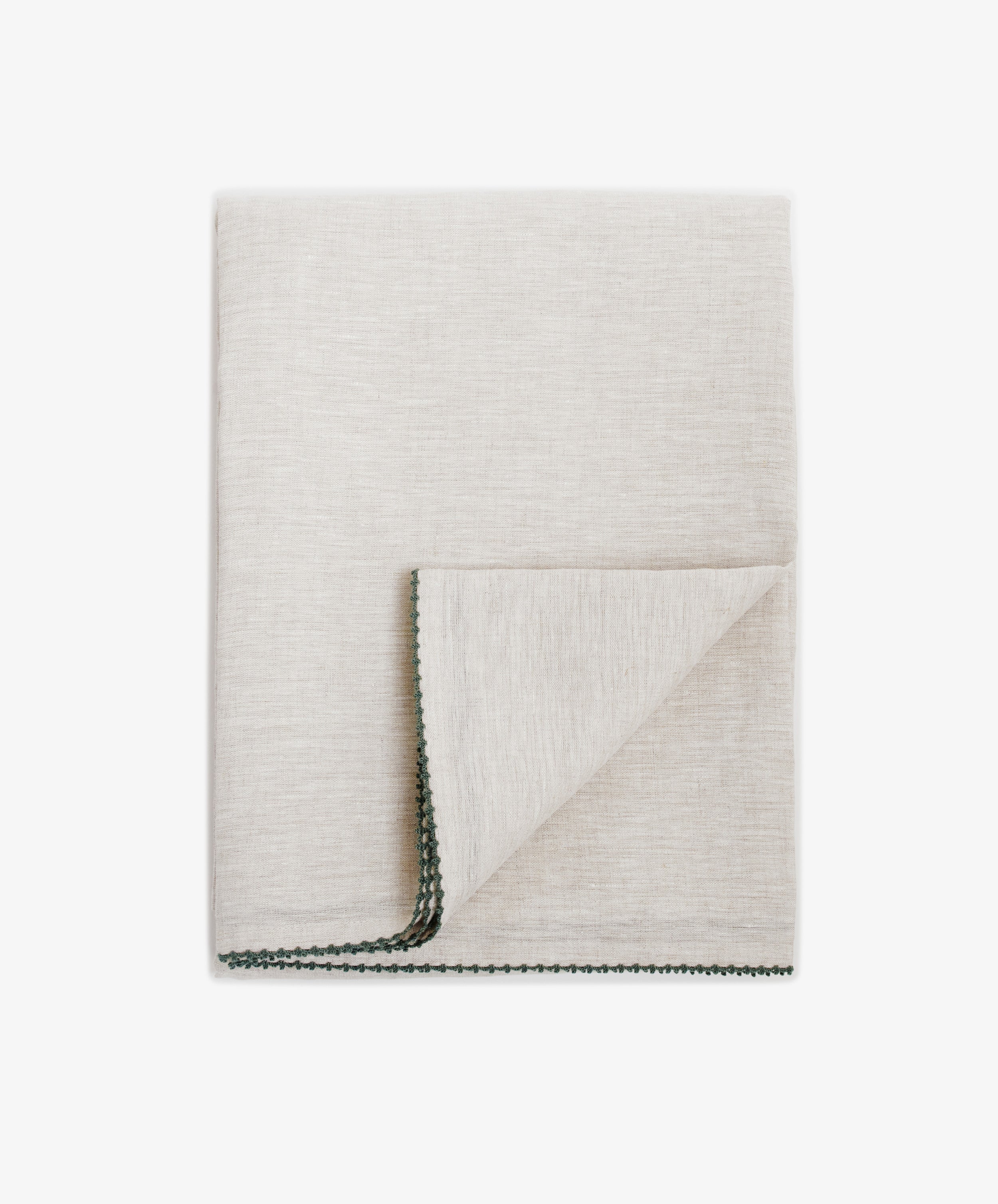 The Nico Tablecloth is shown folded in light beige, featuring visible hand-stitched edging and a flipped corner that reveals the underside.