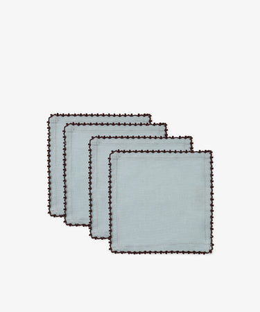 A set of four Nico Cocktail Napkins, each in light blue with dark scalloped edges and a subtle espresso contrast stitch, arranged in a staggered stack on a white background.