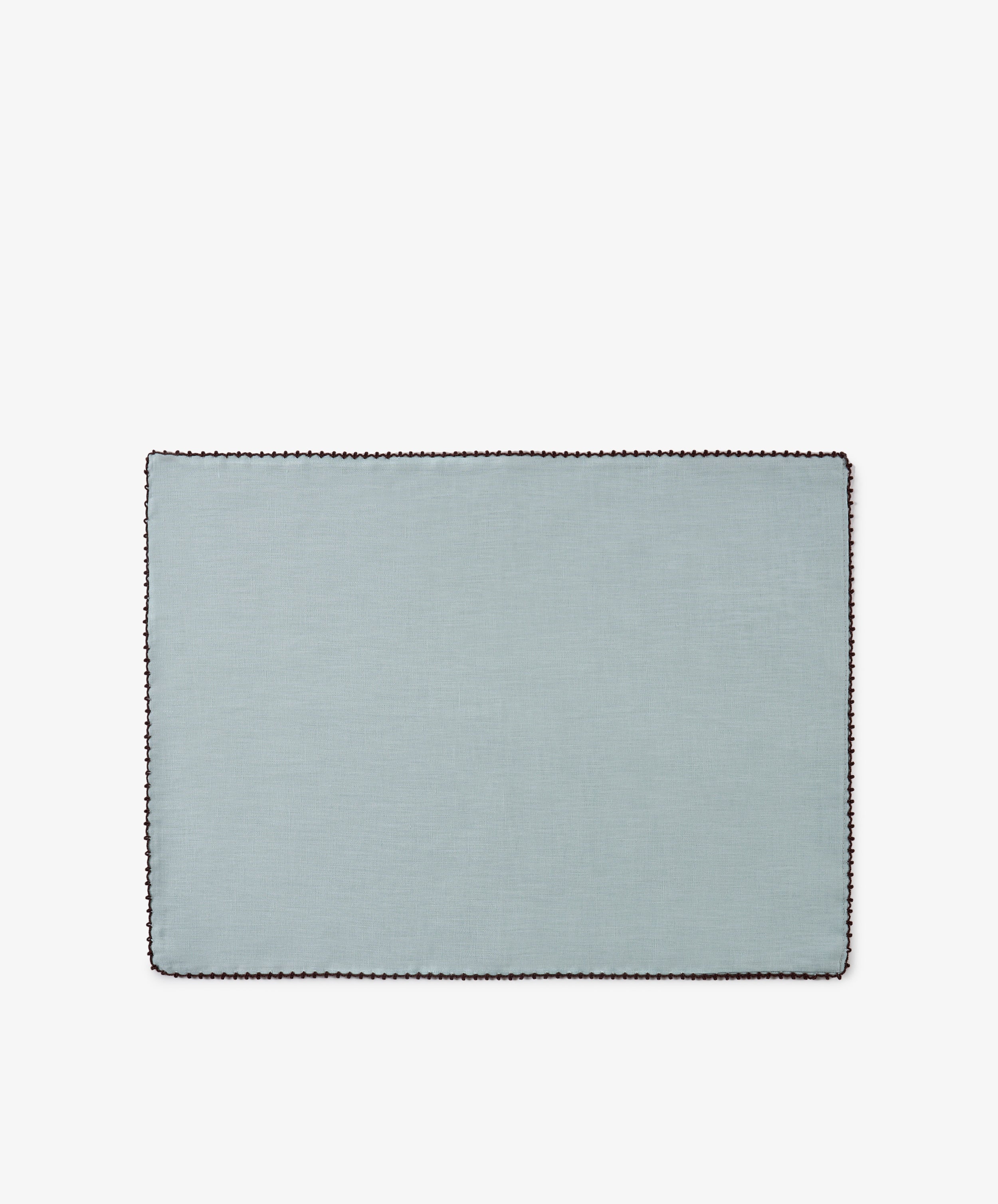 The Nico Placemat, Set of 6, features a rectangular design in light blue Portuguese linen with a dark scalloped border, thoughtfully crafted and displayed on a white background.