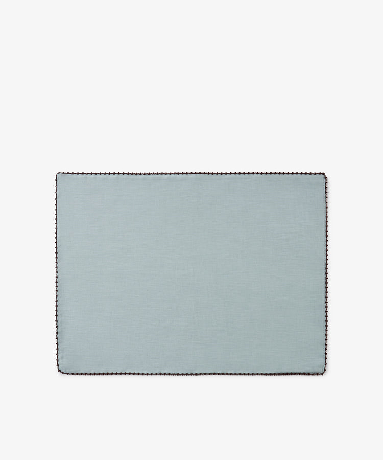 The Nico Placemat, Set of 6, features a rectangular design in light blue Portuguese linen with a dark scalloped border, thoughtfully crafted and displayed on a white background.