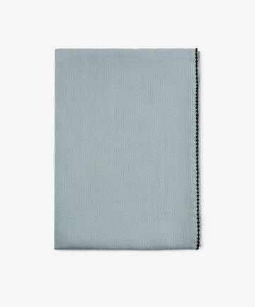 A neatly folded Nico Tablecloth in mint blue with a decorative black stitched edge, displayed against a plain white background. This elegant, hand-finished linen adds a refined touch to any setting.