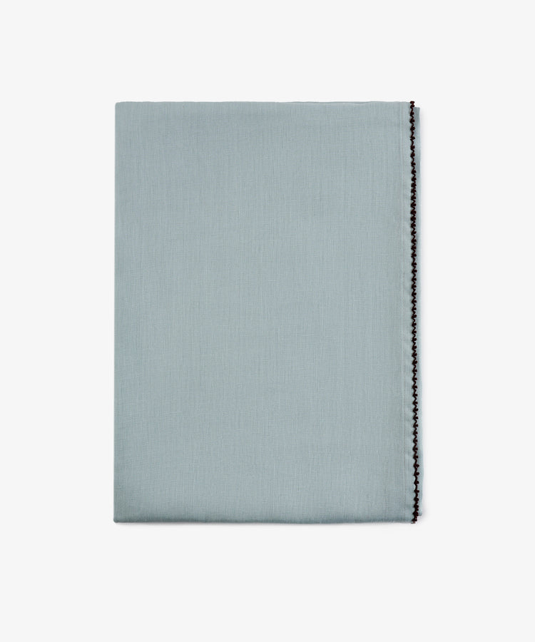 A neatly folded Nico Tablecloth in mint blue with a decorative black stitched edge, displayed against a plain white background. This elegant, hand-finished linen adds a refined touch to any setting.