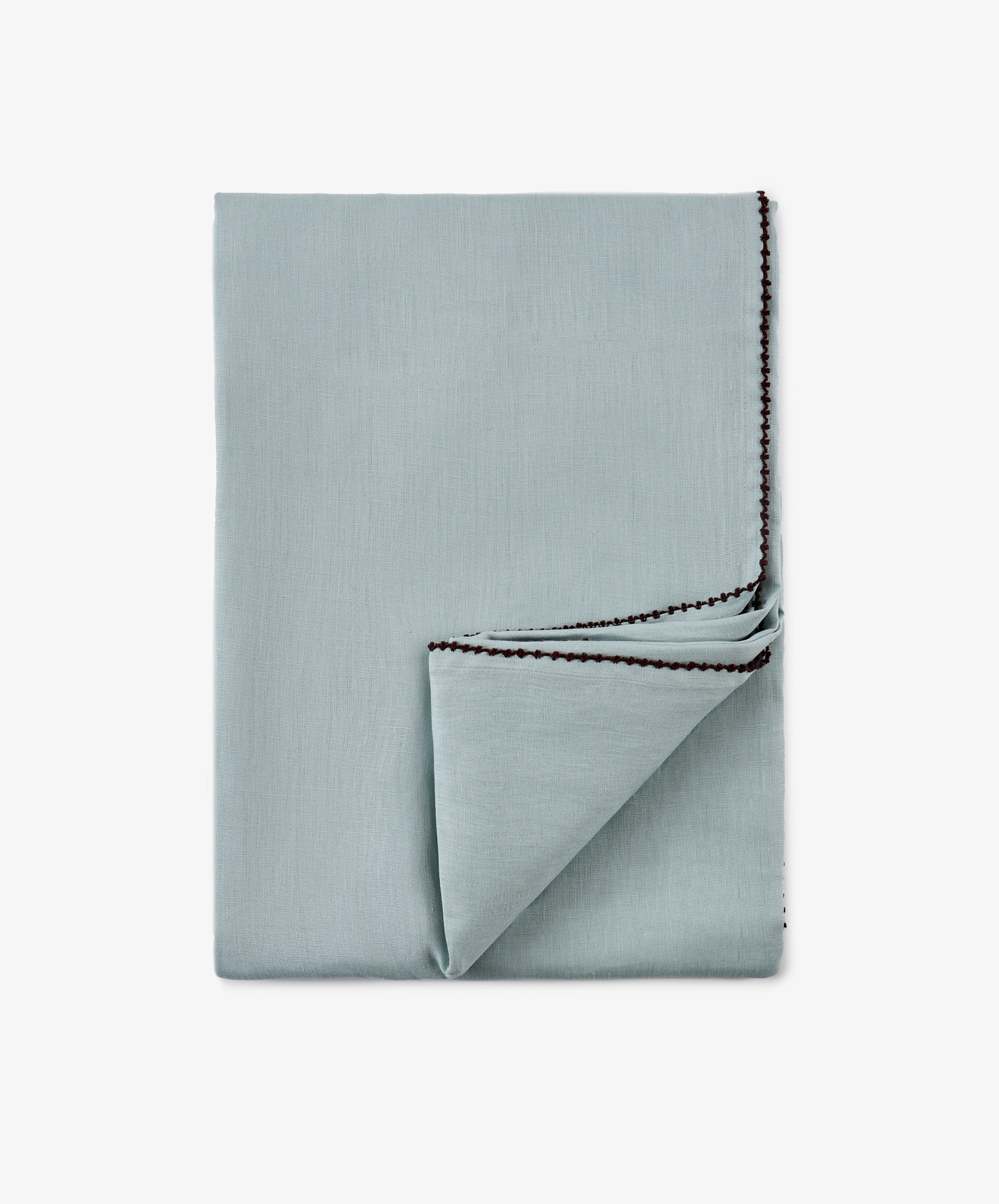 A neatly folded light blue Nico Tablecloth with dark stitched edging, reminiscent of a hand-finished table linen, shown on a plain white background.