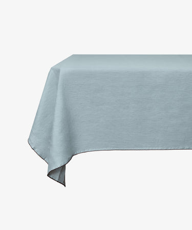 A rectangular table is adorned with the Nico Tablecloth—a mint blue, hand-finished linen piece—displayed against a plain white background.