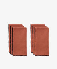Six folded Nico Napkins, set of 6 in rust color with hand-finished black contrast stitching, are arranged in two neat stacks on a white background, highlighting the elegant detailing that accents each linen napkin.