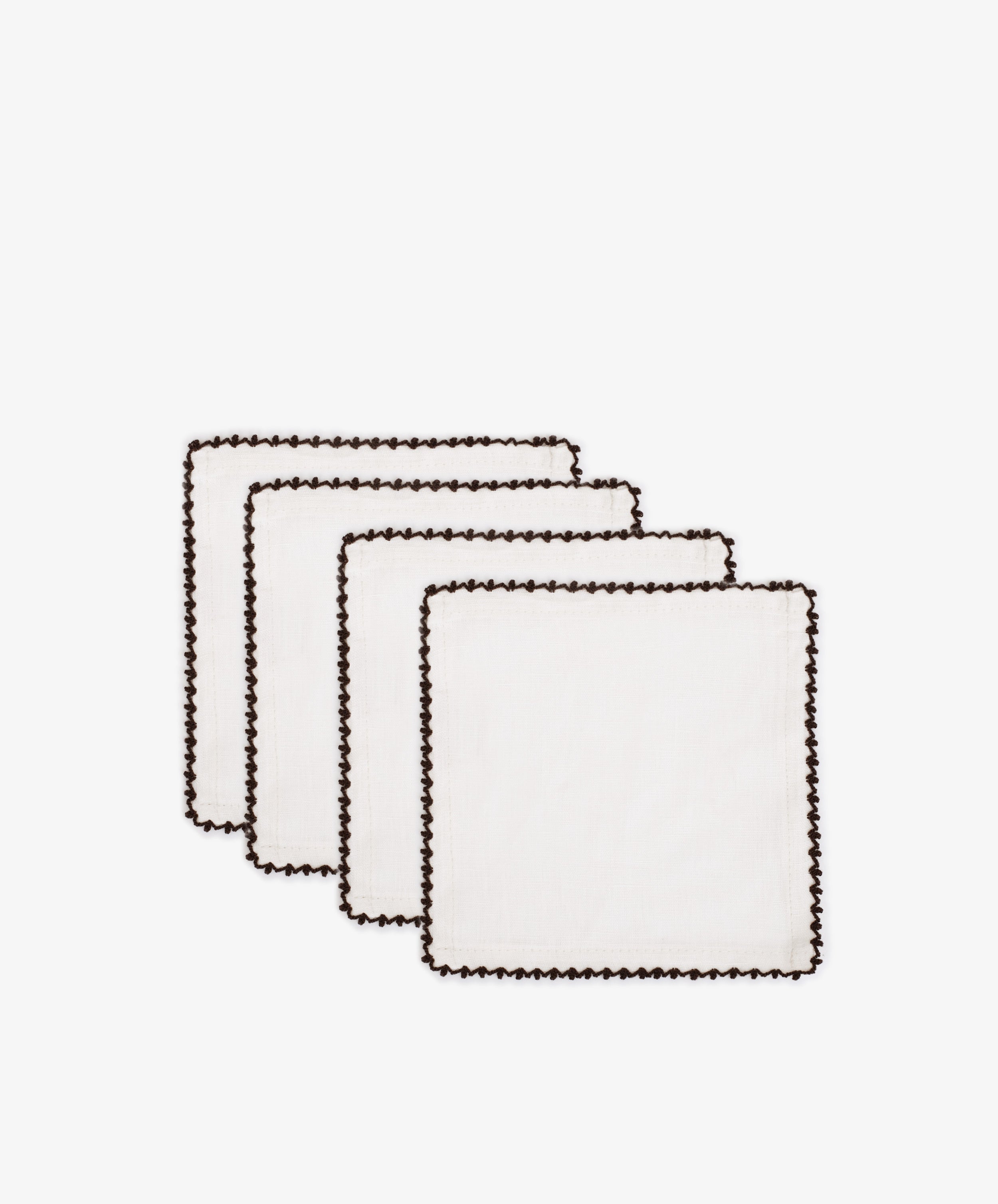 The Nico Cocktail Napkin, Set of 4, features white cloth napkins with hand-finished black contrast stitching and scalloped edges, arranged in an overlapping row on a plain white background.