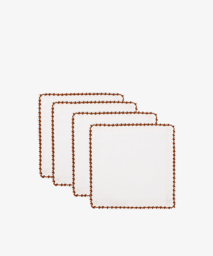 Set of 4 Nico Cocktail Napkins in white, each with brown contrast stitching on the edges, hand-finished and displayed in a staggered row on a white background.