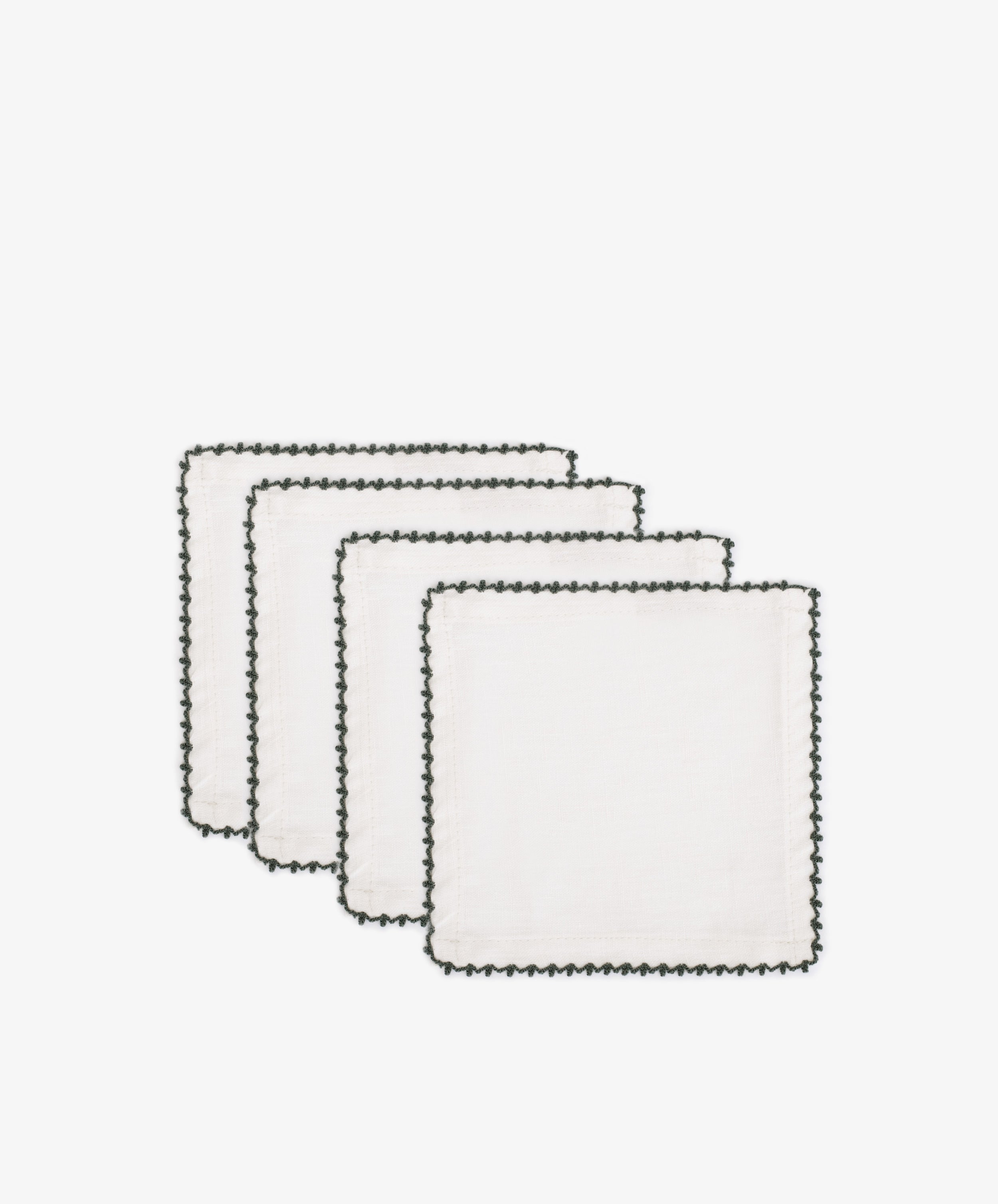 Set of four Nico Cocktail Napkins, featuring white cloth and black hand-finished stitched borders, are stacked in a staggered arrangement against a plain white backgroundâ€”elegant table linens for any occasion.