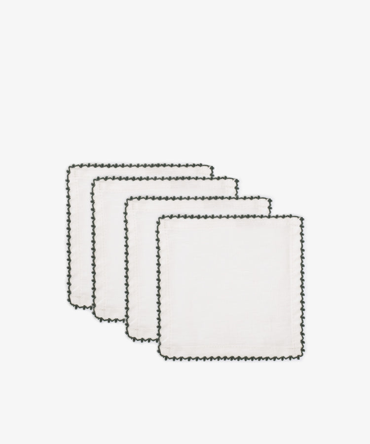 Set of four Nico Cocktail Napkins, featuring white cloth and black hand-finished stitched borders, are stacked in a staggered arrangement against a plain white backgroundâ€”elegant table linens for any occasion.