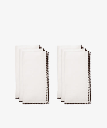 The Nico Napkin, Set of 6, features white cloth napkins with dark scalloped edges, neatly folded and arranged in two stacksâ€”perfect for enhancing any table setting.