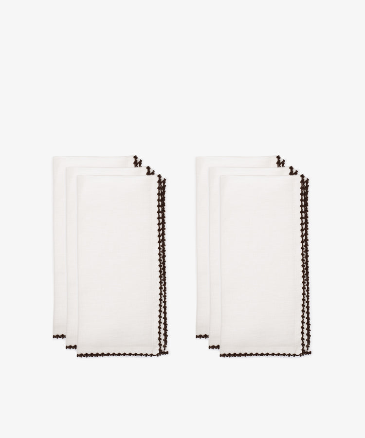 The Nico Napkin, Set of 6, features white cloth napkins with dark scalloped edges, neatly folded and arranged in two stacksâ€”perfect for enhancing any table setting.