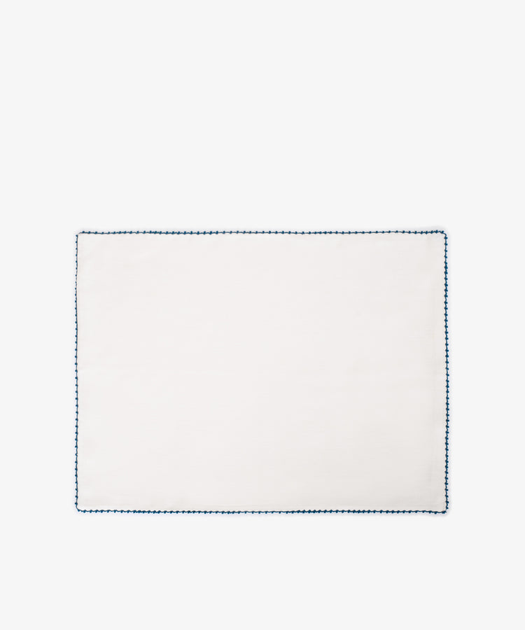 The Nico Placemat, Set of 6, features plain white linen with a blue hand-stitched edge—perfect for adding elegant table decor to any setting. Photographed on a white background.