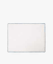 The Nico Placemat, Set of 6, features rectangular white linen with a blue hand-stitched edgeâ€”ideal for adding elegant decor to your table. Displayed on a plain white background.