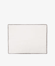 The Nico Placemat, Set of 6, features rectangular white linen mats with hand-stitched edges and a slim dark border—displayed on a plain white background, ideal for creating an elegant Italian-inspired table setting.
