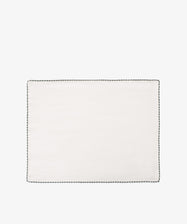 The Nico Placemat, Set of 6, features rectangular white linen with a black hand-stitched edge, shown on a white backgroundâ€”ideal for adding Italian elegance to your table.