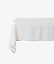 The Nico Tablecloth, made from white linen with subtle red contrast stitching, is elegantly draped over a table and set against a plain white background.