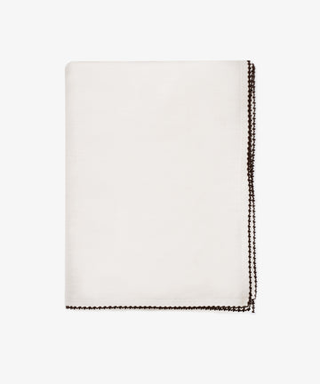 The Nico Tablecloth, featuring contrast stitching along its dark decorative border, is neatly folded and displayed on a plain white background.