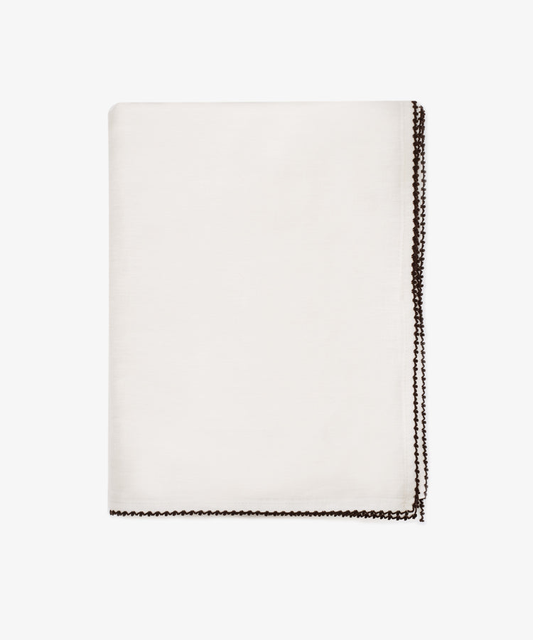 The Nico Tablecloth, featuring contrast stitching along its dark decorative border, is neatly folded and displayed on a plain white background.