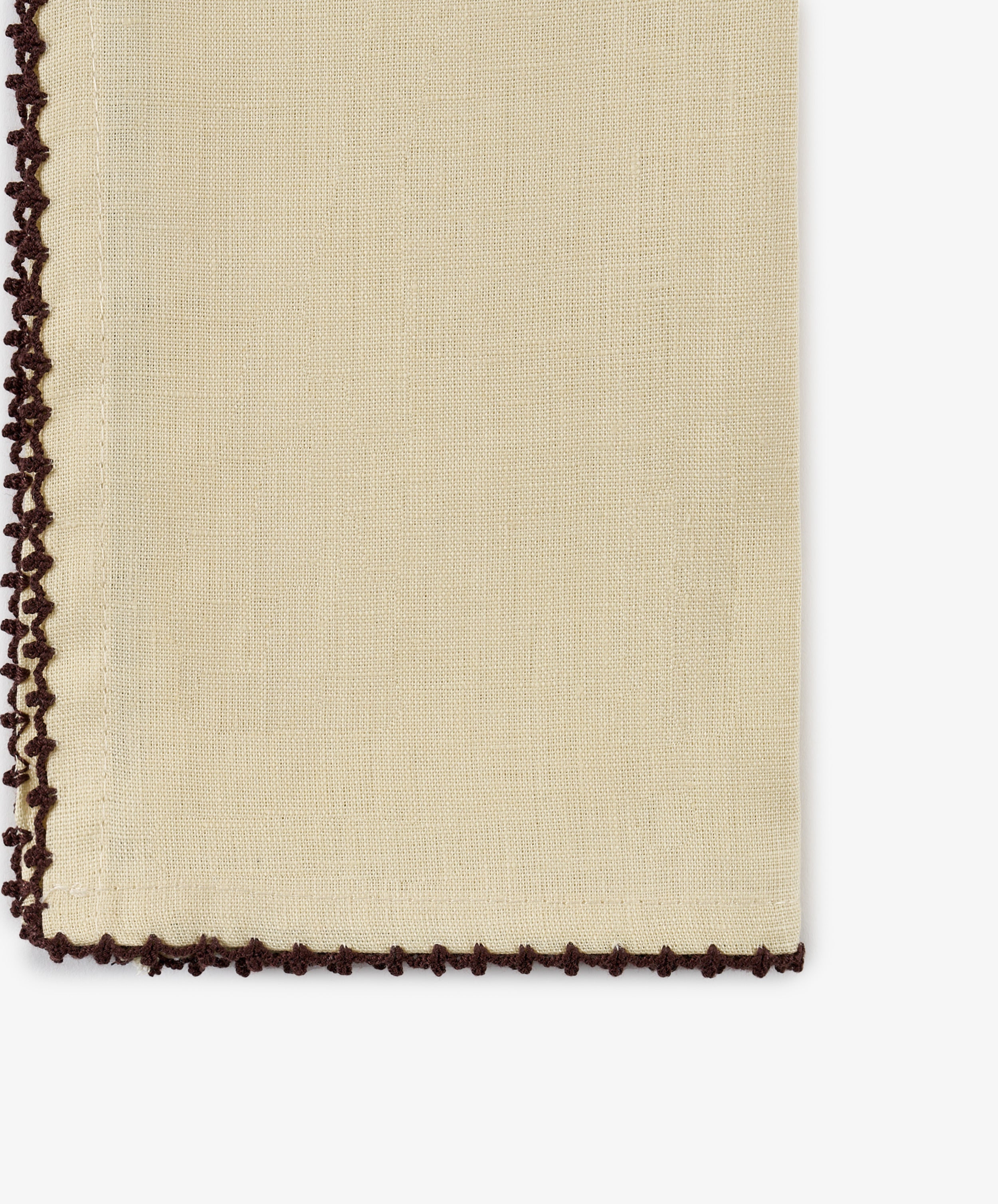 A close-up of the Nico Napkin, Set of 6, in a beige linen fabric with dark brown crochet trim along the left and bottom edges, featuring antique-inspired espresso contrast stitch details.
