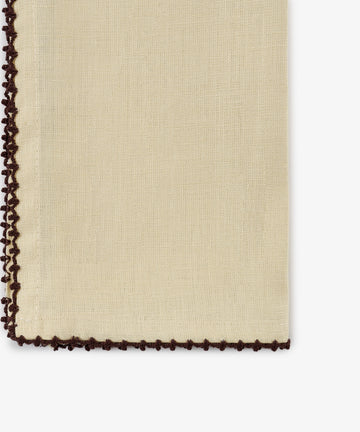 A close-up of the Nico Napkin, Set of 6, in a beige linen fabric with dark brown crochet trim along the left and bottom edges, featuring antique-inspired espresso contrast stitch details.