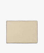 The Nico Placemat, Set of 6 features a rectangular design in beige linen with an espresso stitch border in a contrasting dark color, hand finished for a refined touch, and displayed on a plain white background.