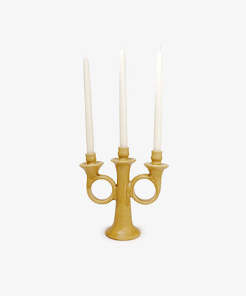 The Loretta Candelabra is a yellow handmade ceramic piece with three holders, each displaying a tall white taper candle, radiating Old World charm against a plain white background.