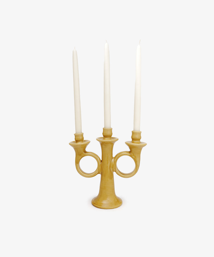 The Loretta Candelabra is a yellow handmade ceramic piece with three holders, each displaying a tall white taper candle, radiating Old World charm against a plain white background.