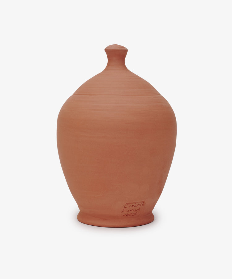 The Hugo Money Pot is a terracotta clay jar with a fitted lid, smooth rounded shape, and a small inscription near the base. This sculptural coin bank is shown against a plain white background.