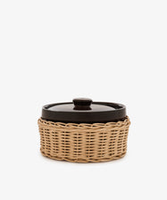 Amany Casserole, a black-lidded ceramic baking dish nestled in a round woven rattan basket, photographed against a plain white background.
