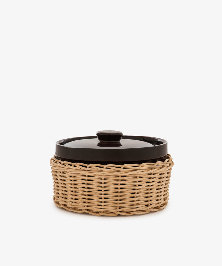 Amany Casserole, a black-lidded ceramic baking dish nestled in a round woven rattan basket, photographed against a plain white background.