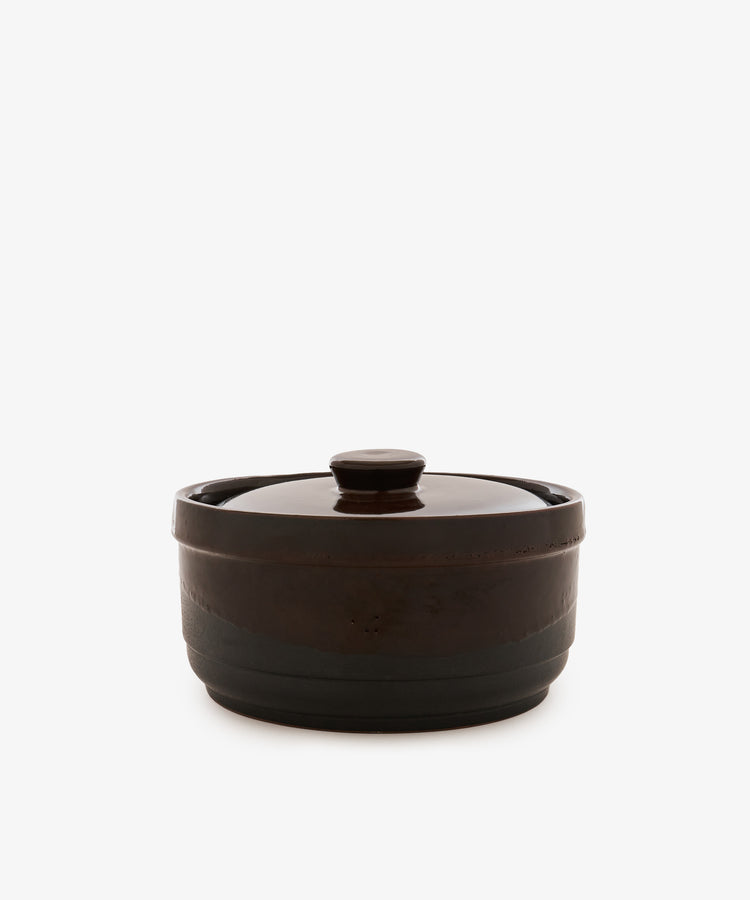 The Amany Casserole, a round, dark brown ceramic baking dish with a lid, is centered on a plain white background.