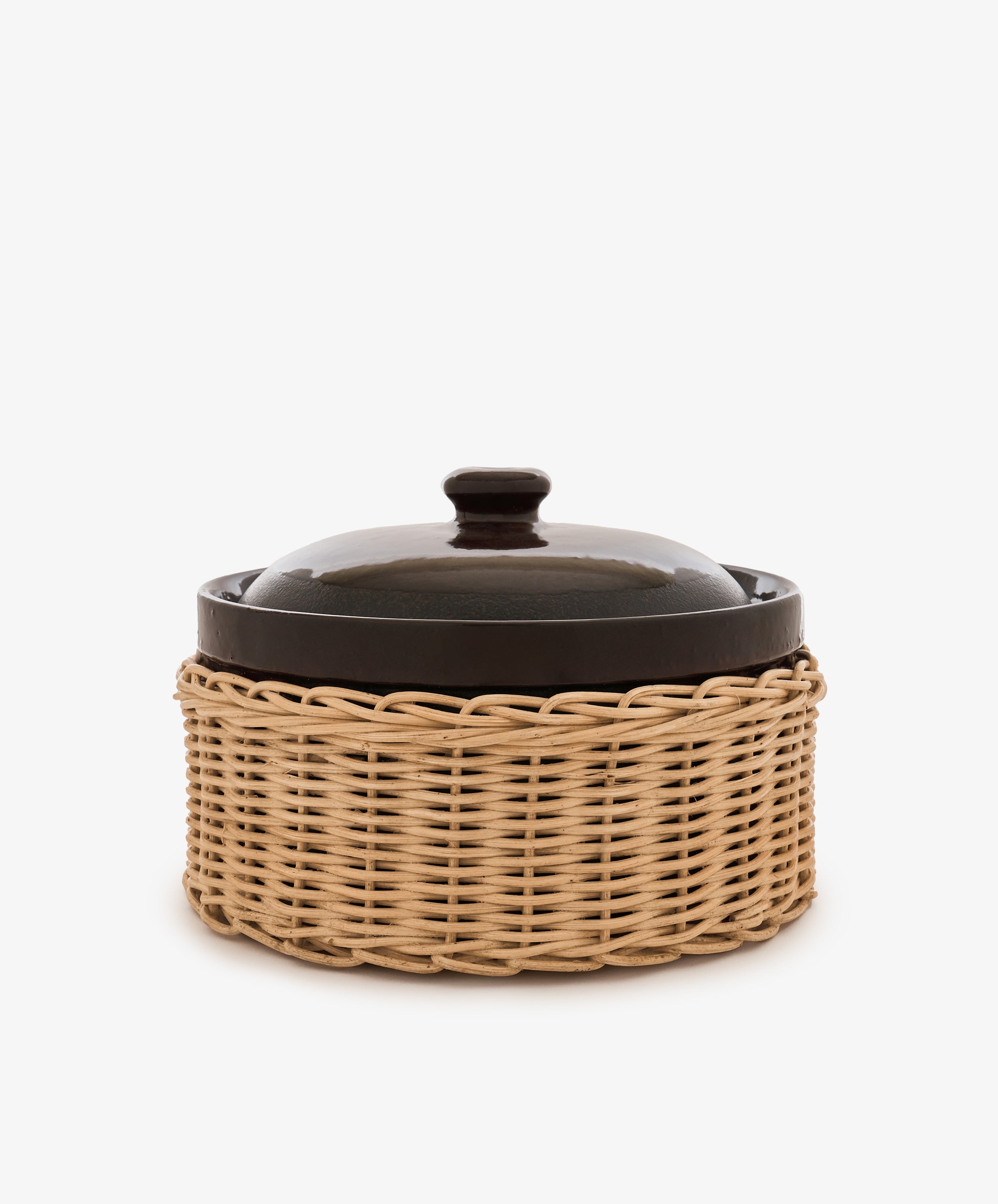 The Amany Casserole, a dark stoneware dish with a lid, is presented inside a light-colored woven wicker basket against a plain white background.