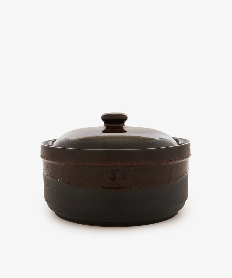 The Amany Casserole is a dark, round ceramic baking dish featuring a matching lid with a knob handle, displayed against a plain white background.