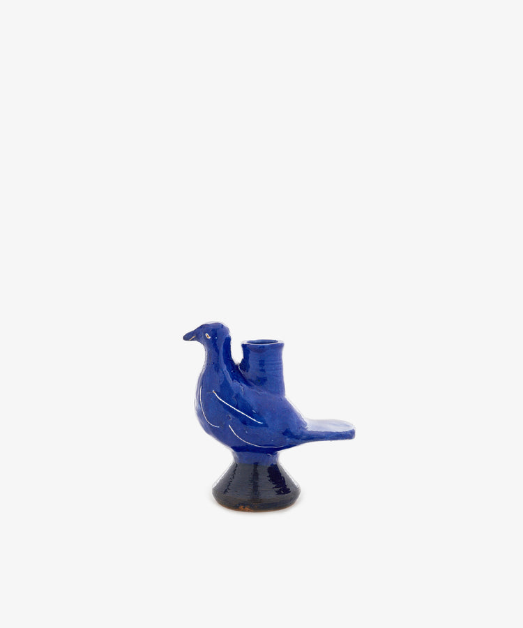 The Peace Dove Candle Holder is a blue ceramic ornament finished with a rich cobalt glaze. Featuring a cylindrical holder on its back, this charming pedestal piece sits gracefully on a plain white background, combining whimsical design with vibrant color to brighten any space.