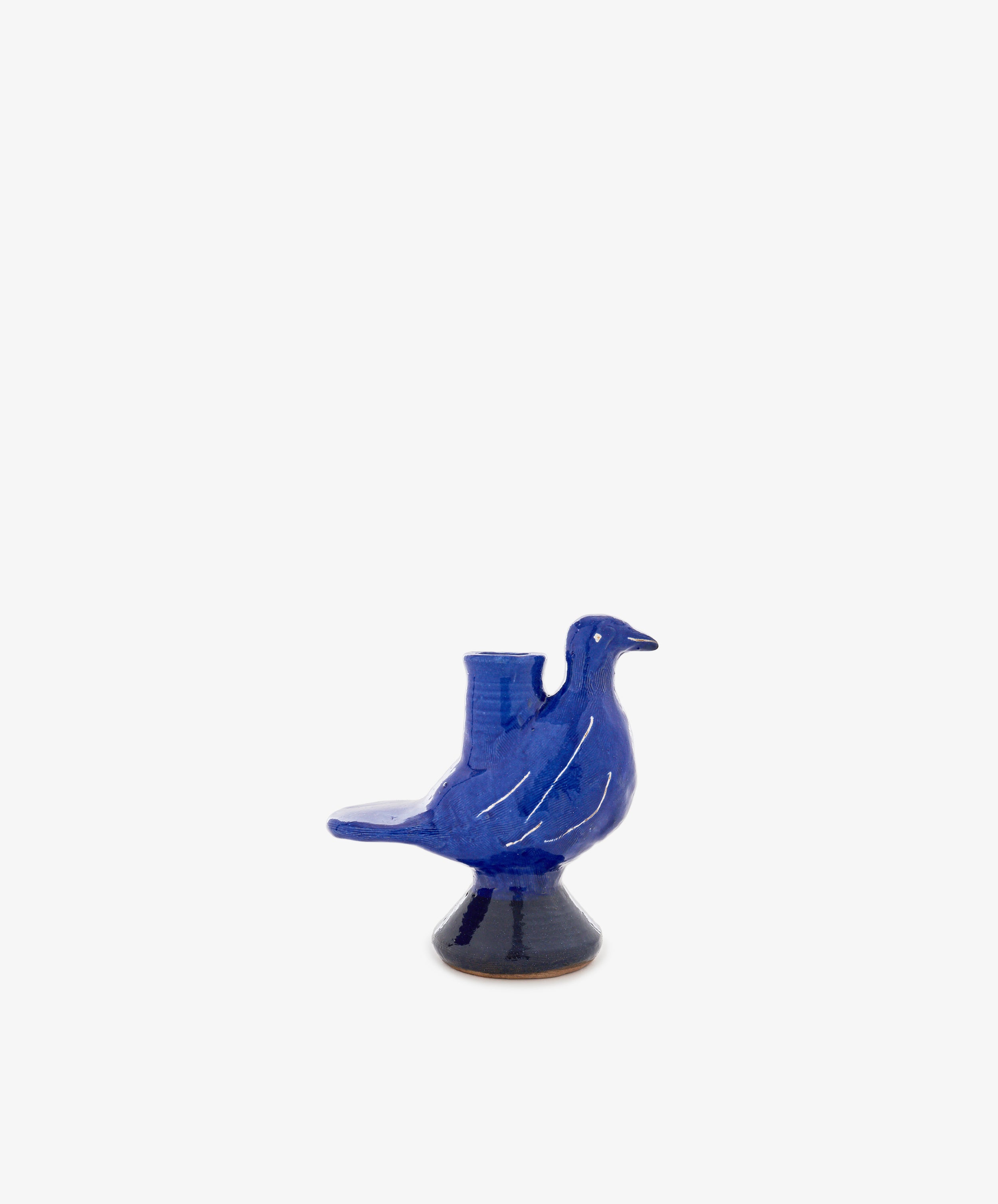 The Peace Dove Candle Holder is a blue ceramic bird with a beautiful cobalt glaze, standing on a small round pedestal ornament against a plain white background.