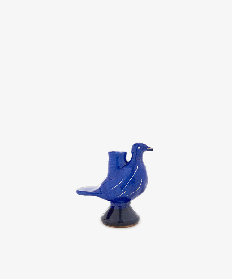 The Peace Dove Candle Holder is a blue ceramic bird with a beautiful cobalt glaze, standing on a small round pedestal ornament against a plain white background.